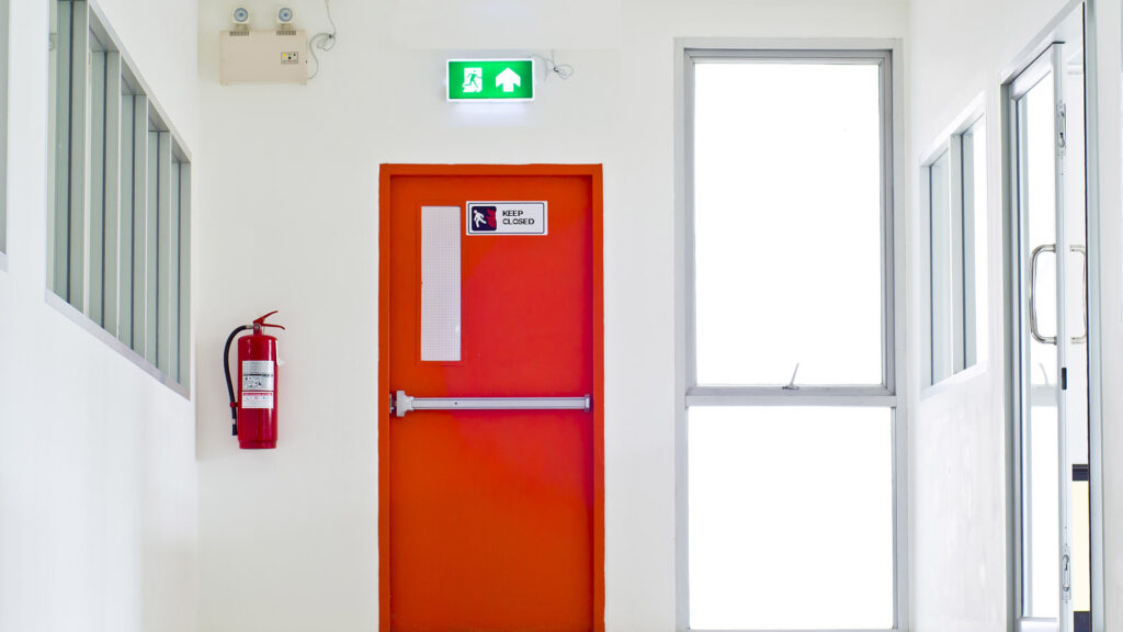 Fire exit door fitted with safety signage and fire door hardware in a commercial building corridor.